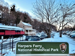Un panneau indiquant le parc historique national de Harpers Ferry, avec en arrière-plan une rue enneigée et des voitures garées.