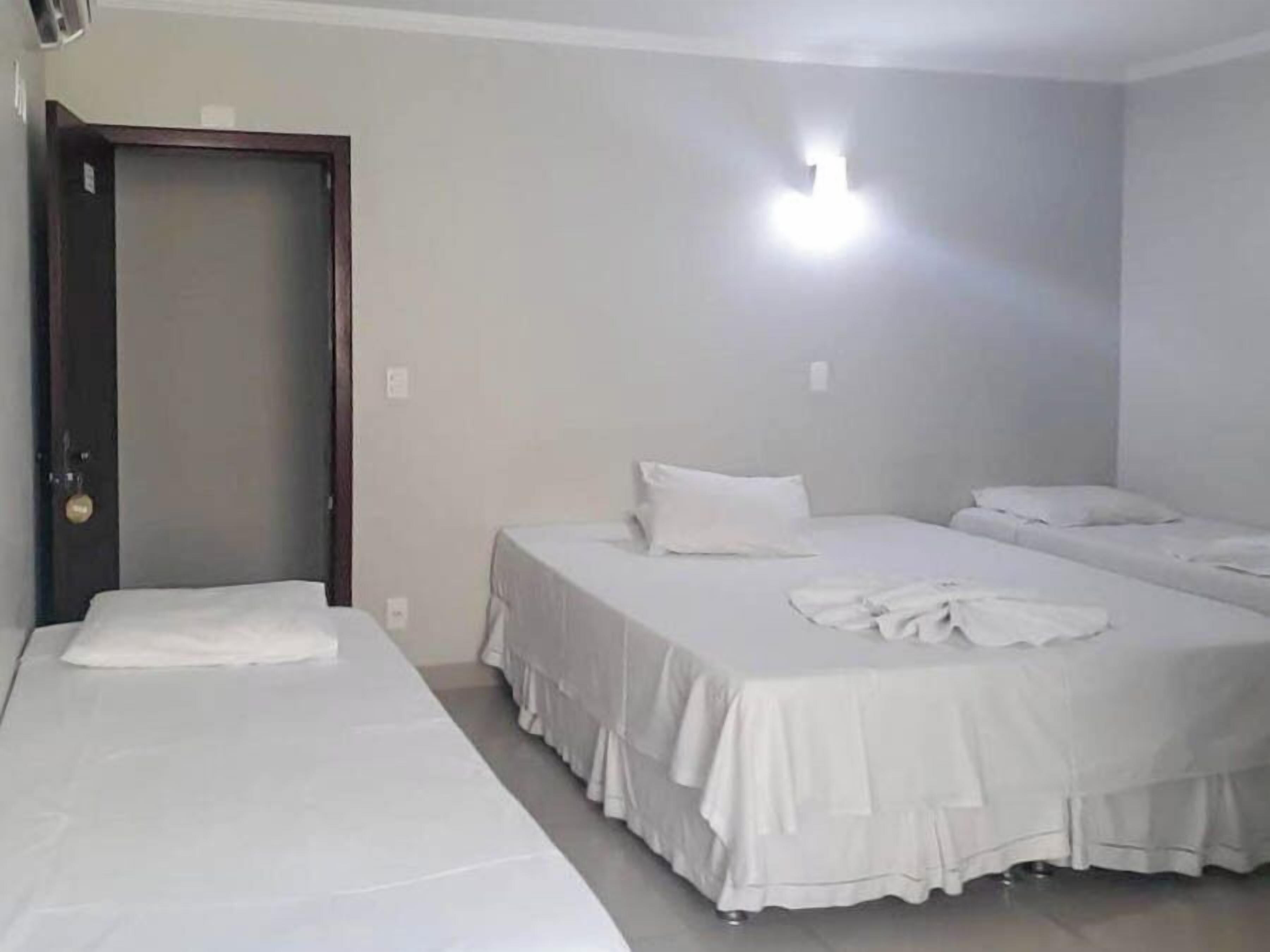 Habitación de hotel con dos camas individuales, una puerta y una lámpara en la pared.