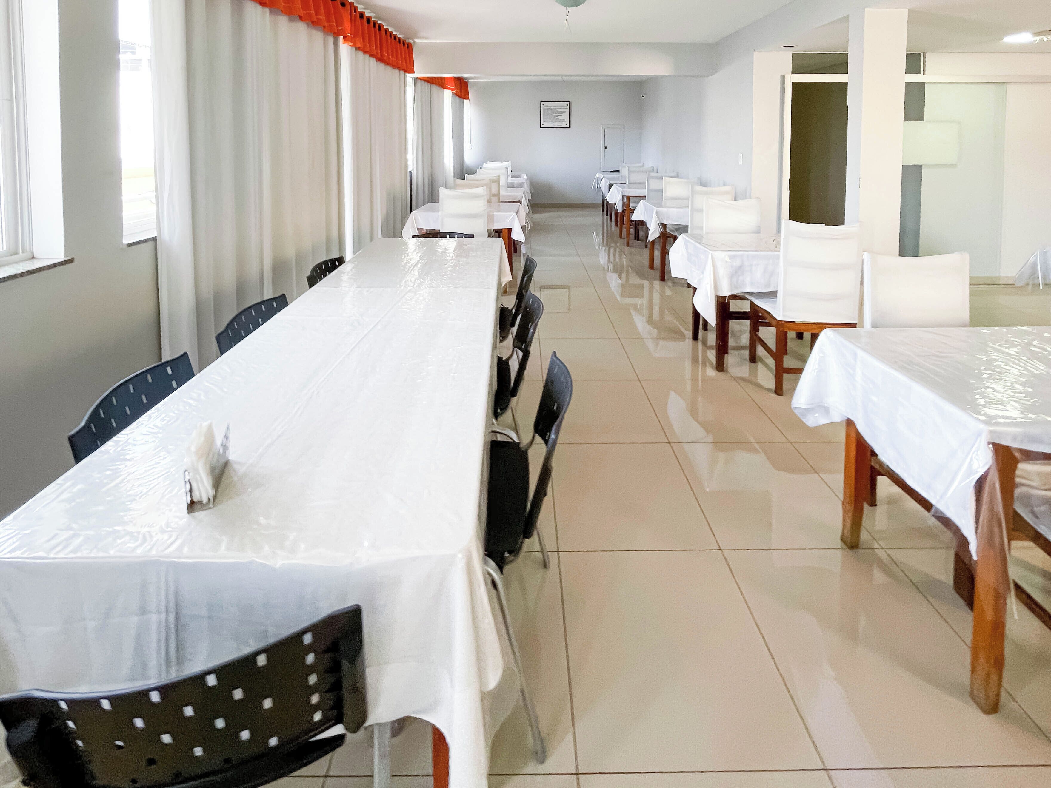 A long dining hall with tables and chairs, a tiled floor, and a door in the background.