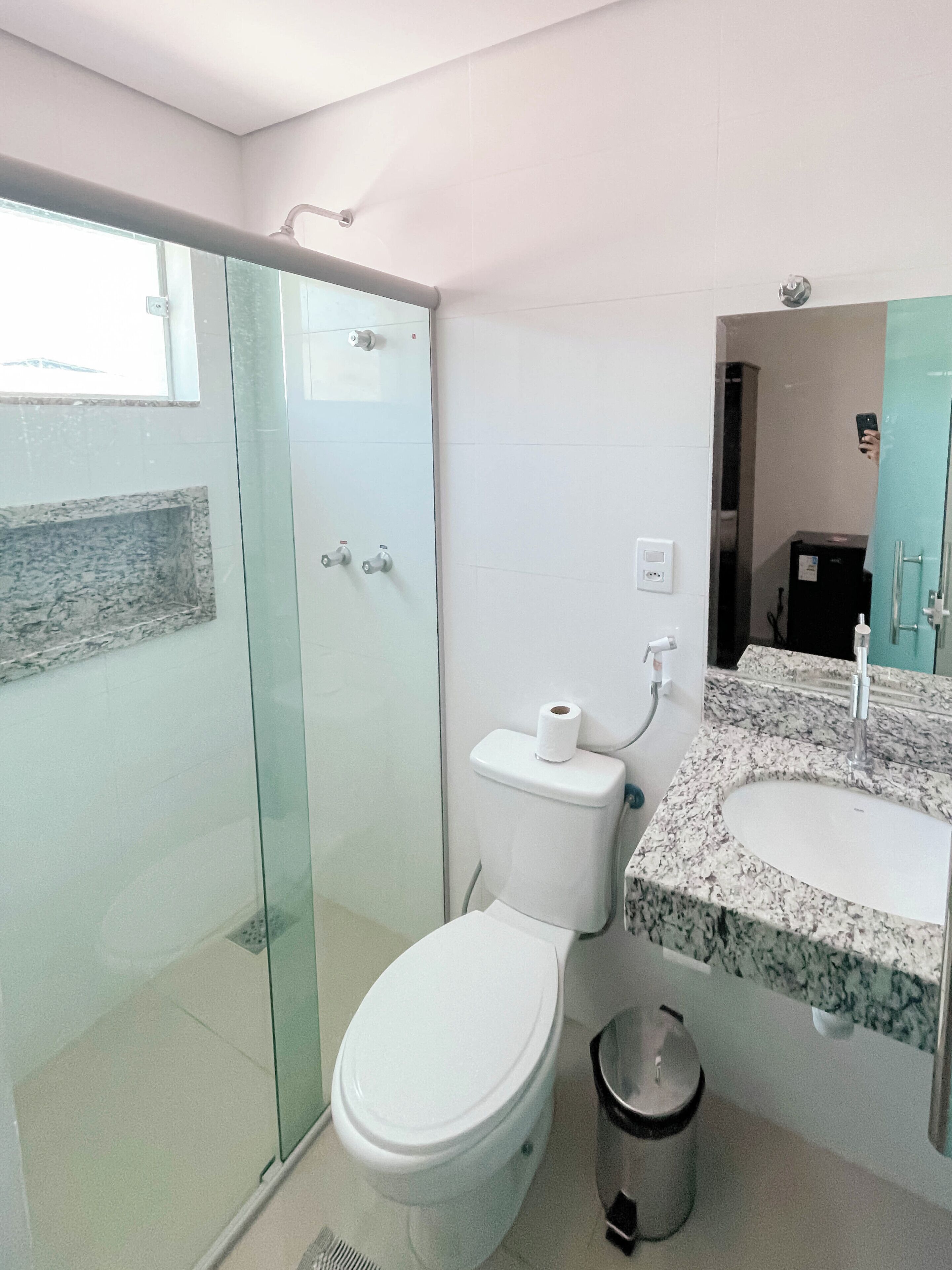 A modern bathroom with a glass shower enclosure, a white toilet, a granite countertop sink, and a mirror above the sink.