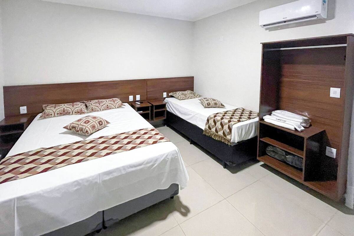 Habitación de hotel con dos camas individuales, un armario y un equipo de aire acondicionado.