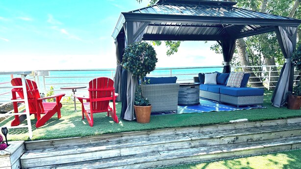 A covered outdoor seating area with a view of the ocean, featuring a wooden deck, red Adirondack chairs, and a blue sofa.