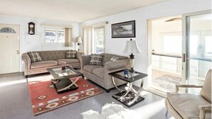 A living room with a sofa set, a coffee table, a lamp, and a view through a glass door.