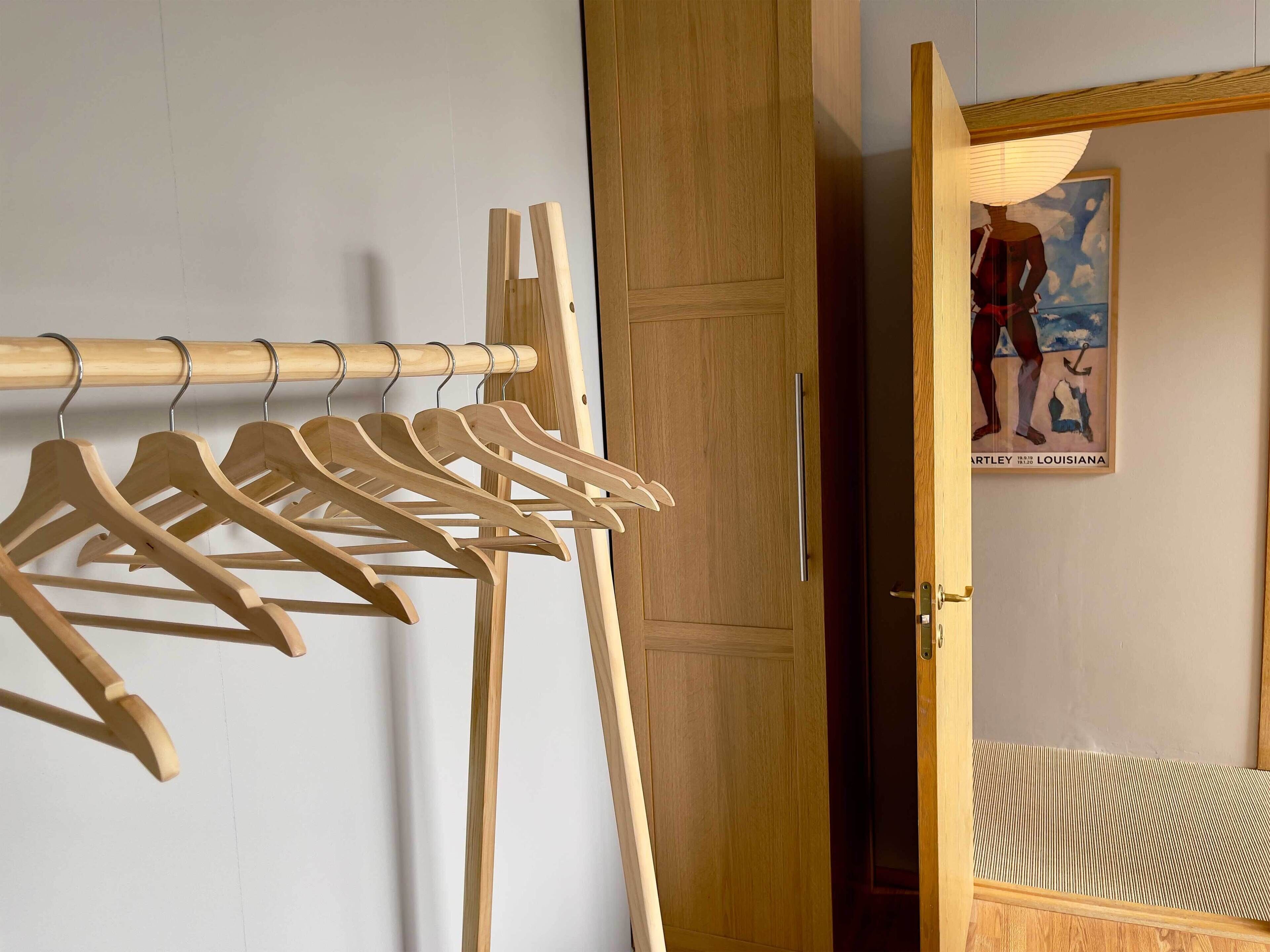 A wooden clothing rack with hangers, a wooden door, and a bed with a striped bedspread.