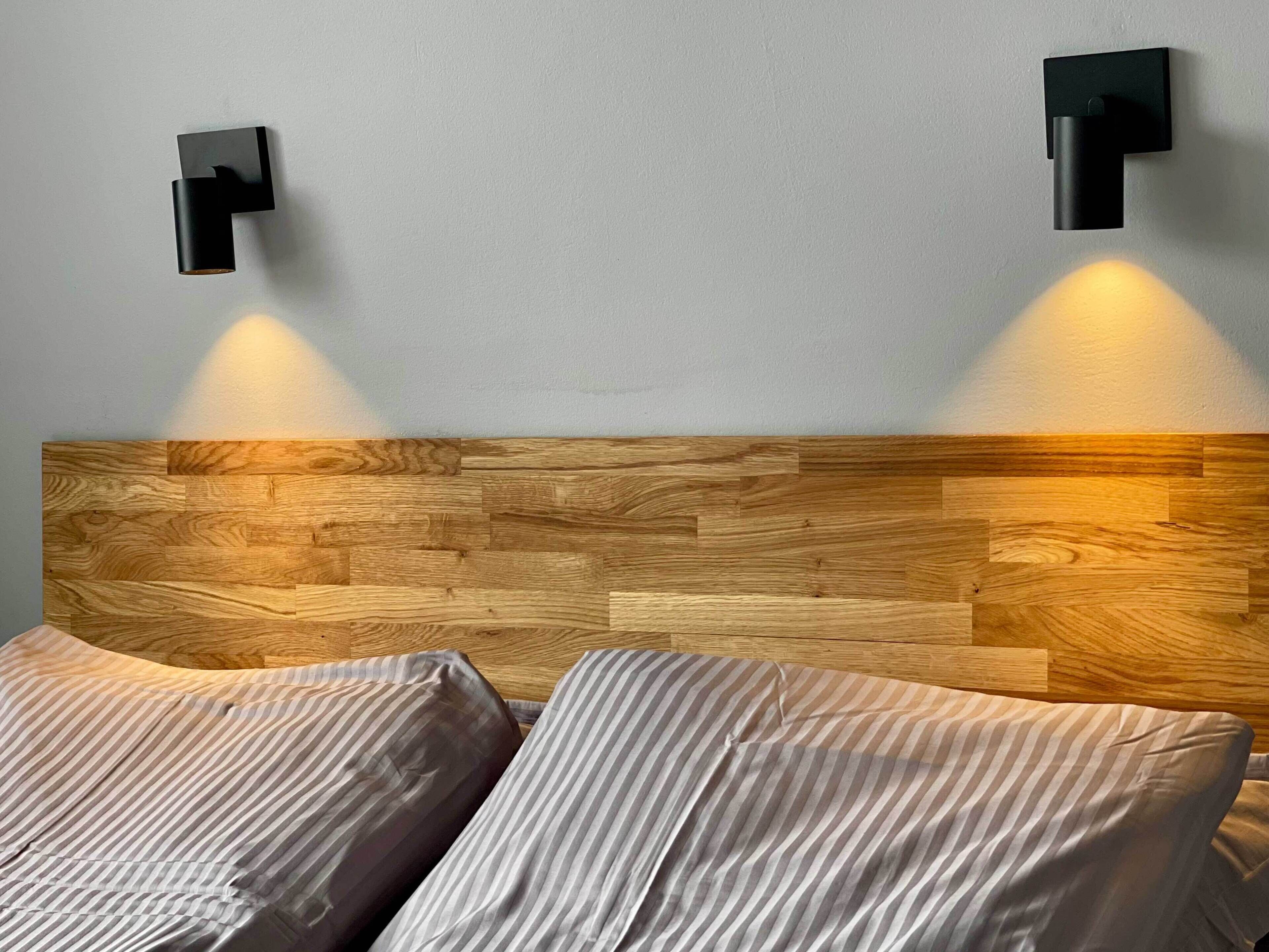 A bedroom with a wooden headboard, two bedside tables, and two wall-mounted lights.