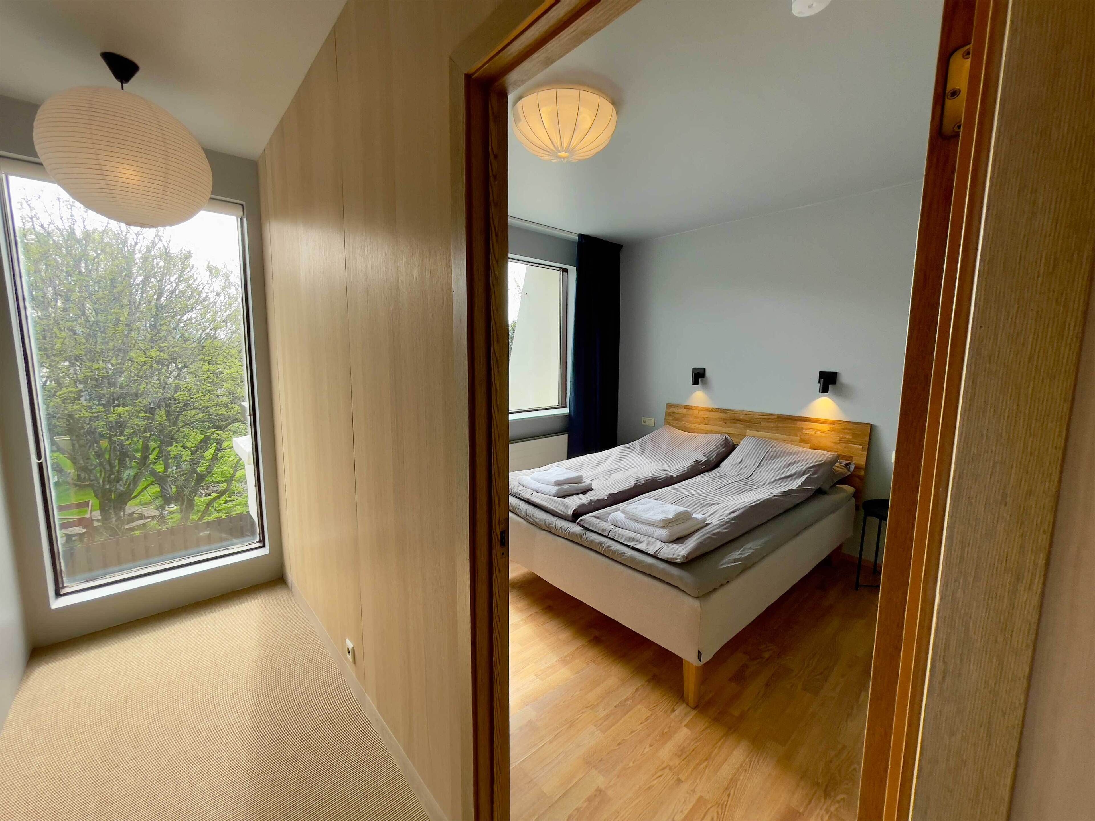 A modern bedroom with a large window, a bed with a wooden headboard, and a ceiling light fixture.