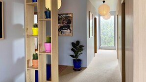 Un pasillo con una estantería de madera, plantas en macetas, un cartel y un ventanal grande.