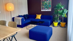 Una sala de estar moderna con un sofá azul, una mesa de centro, una mesa de comedor de madera y plantas en macetas.