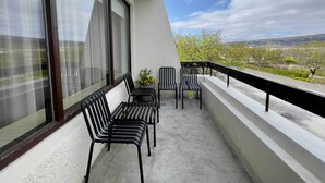 Un balcón con mesa y sillas, una planta en maceta y vistas a árboles y colinas.