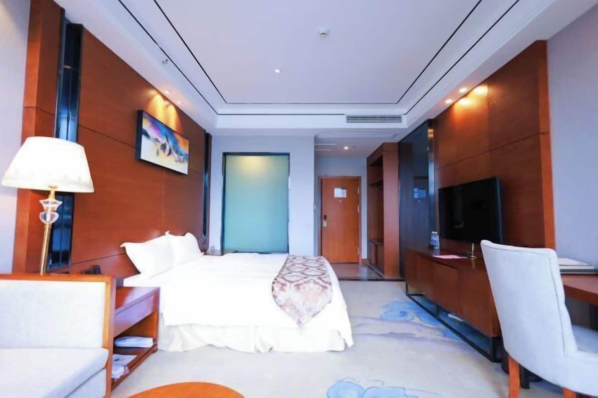 A hotel room with a bed, a desk, a chair, a TV, and a painting on the wall.