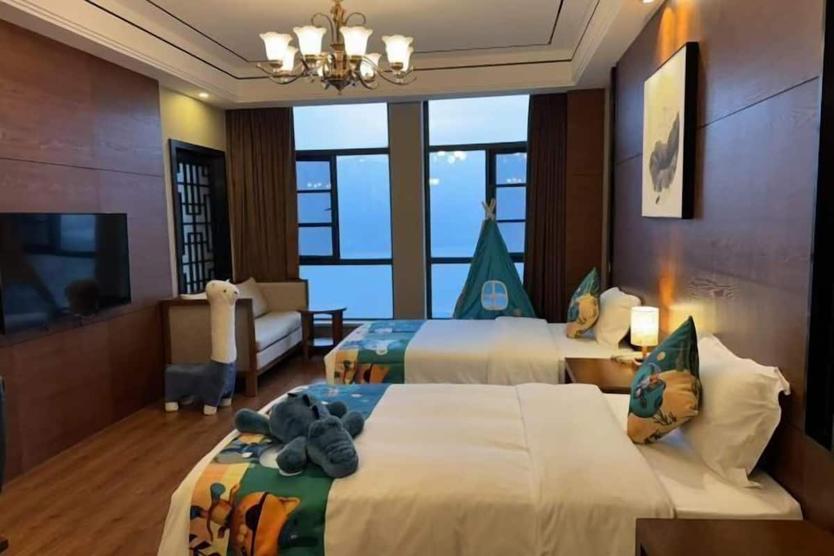 A hotel room with two beds, a sofa, a TV, and a view of the sky.
