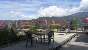 Un área de estar al aire libre con mesas y sillas, rodeada de banderas rojas y un paisaje montañoso.