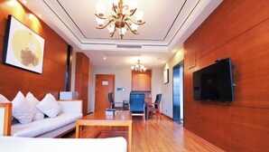 Una habitación de hotel con piso de madera, un sofá, un televisor y una araña.