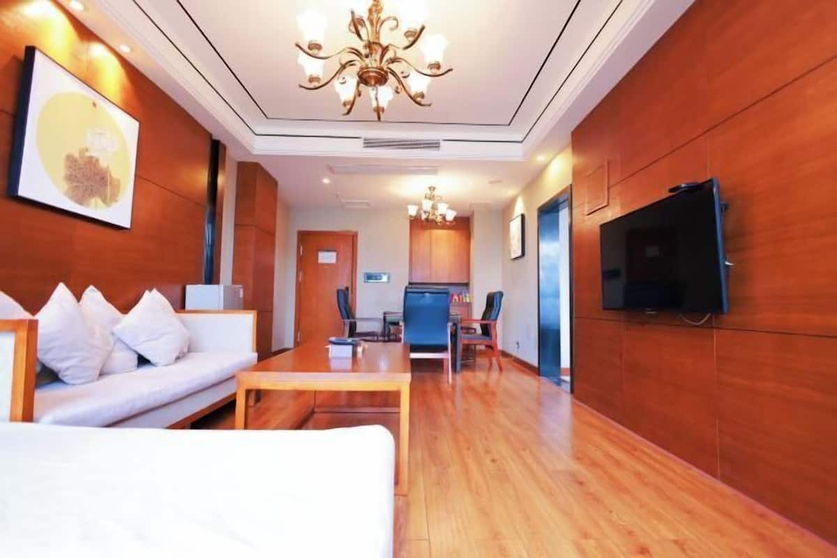A hotel room with a wooden floor, a sofa, a TV, and a chandelier.