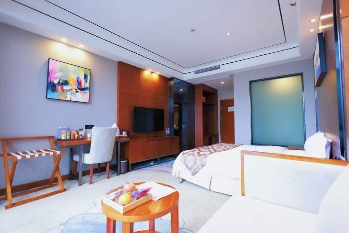 A modern hotel room with a bed, desk, chair, TV, and artwork on the wall.