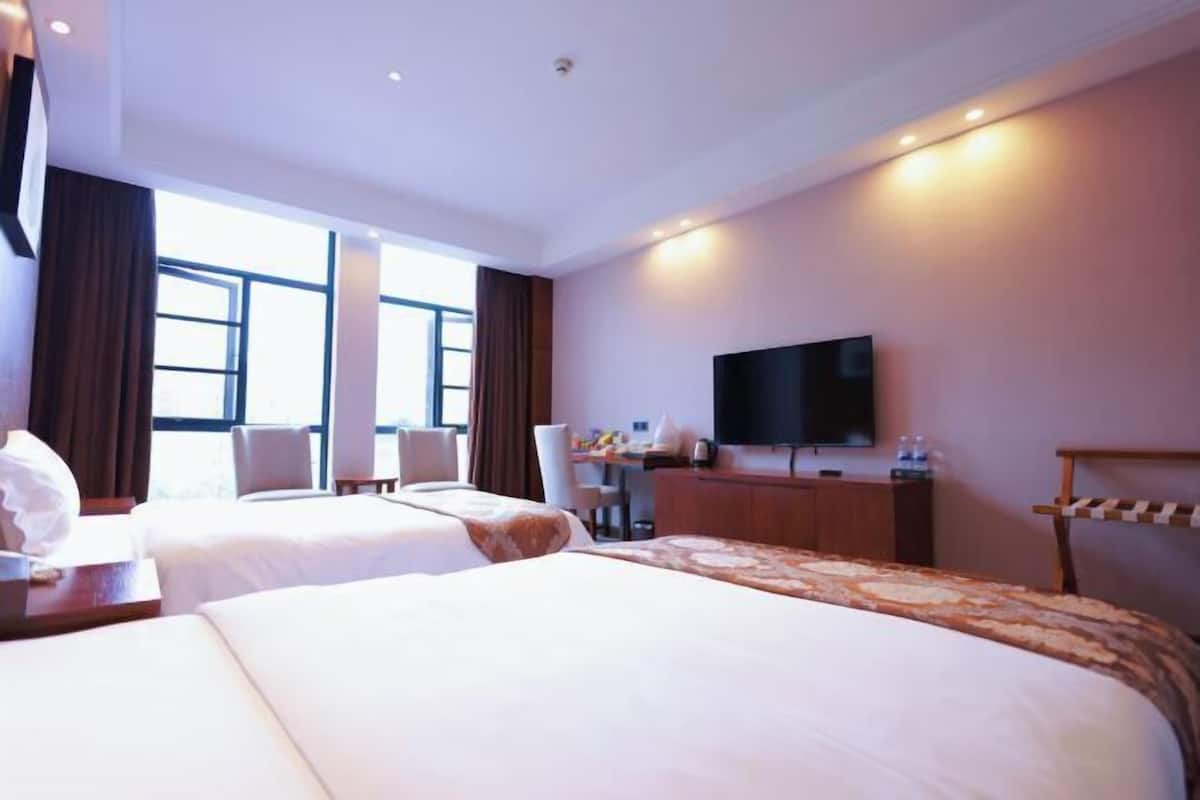 A hotel room with two beds, a desk, a chair, a TV, and a window.