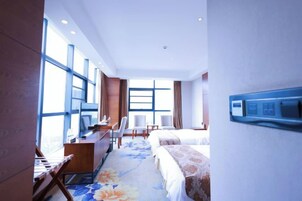 Una habitación de hotel con escritorio, sillas, cama y ventanas amplias.