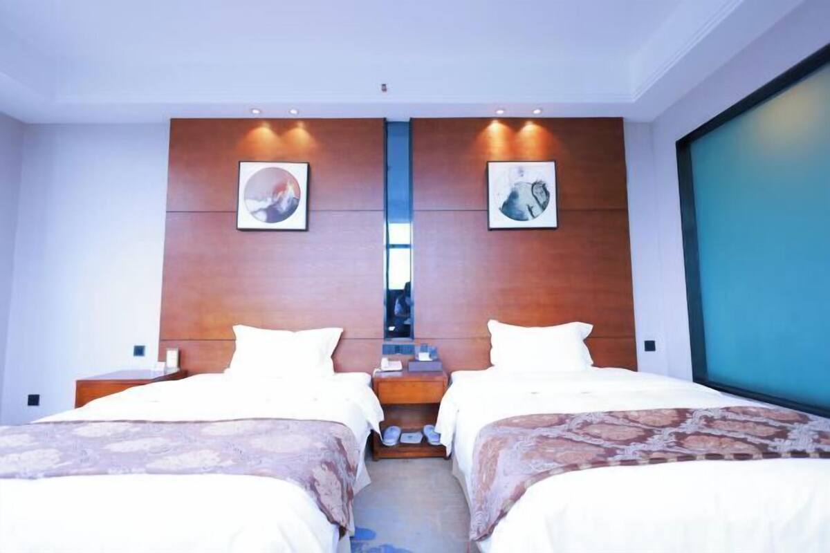 A hotel room with two beds, a wooden headboard, artwork, and a large window.