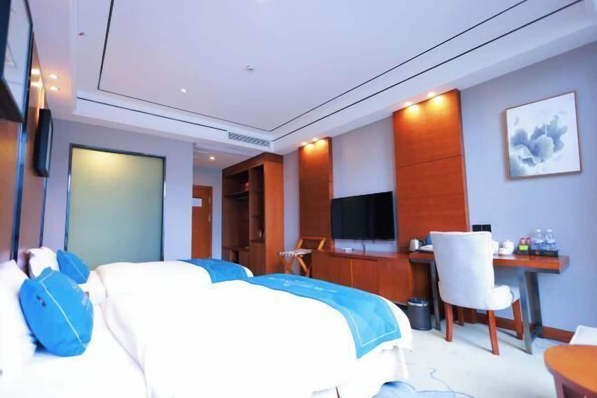 A hotel room with a bed, a desk, a chair, a TV, and a painting on the wall.