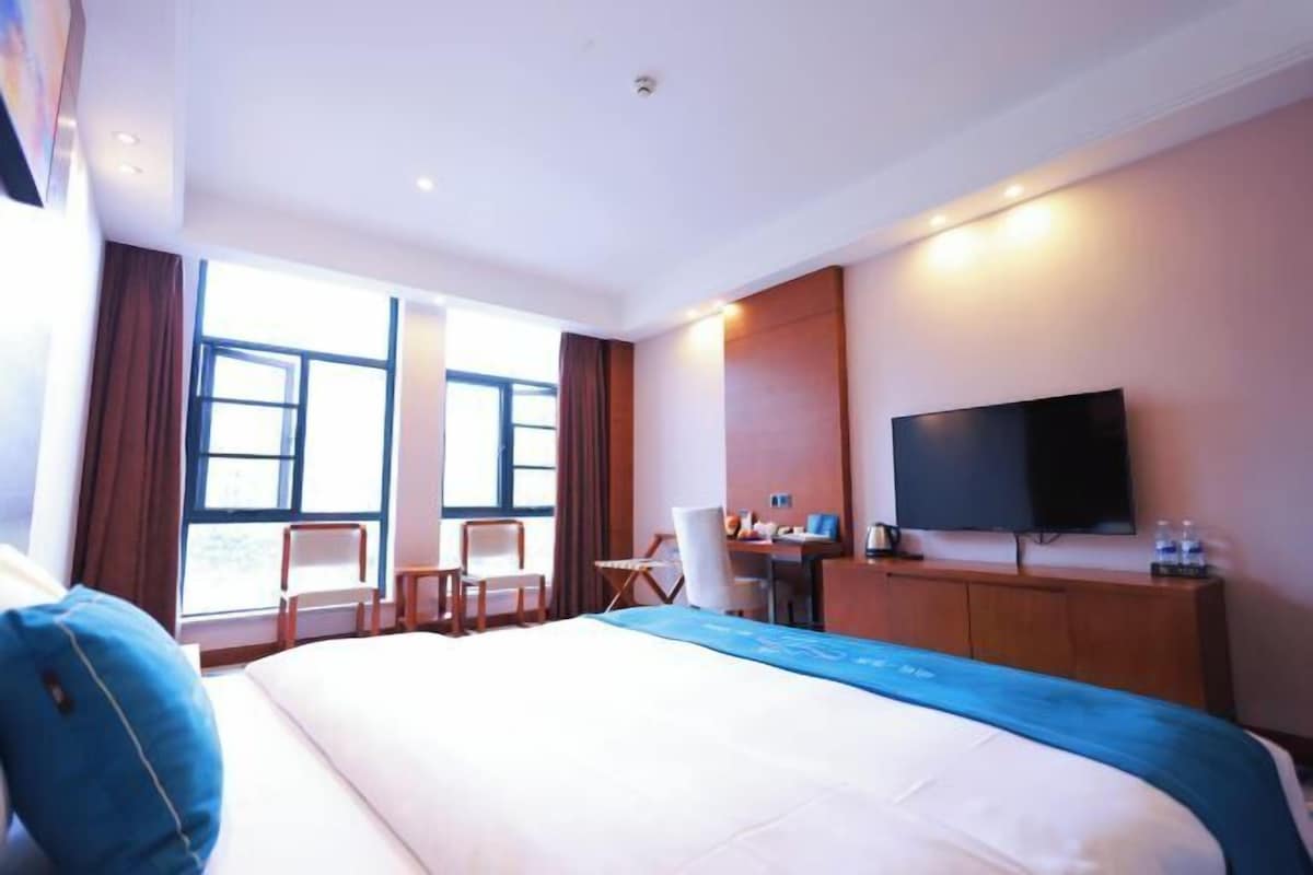 A hotel room with a large bed, a desk, a chair, a TV, and a window with curtains.