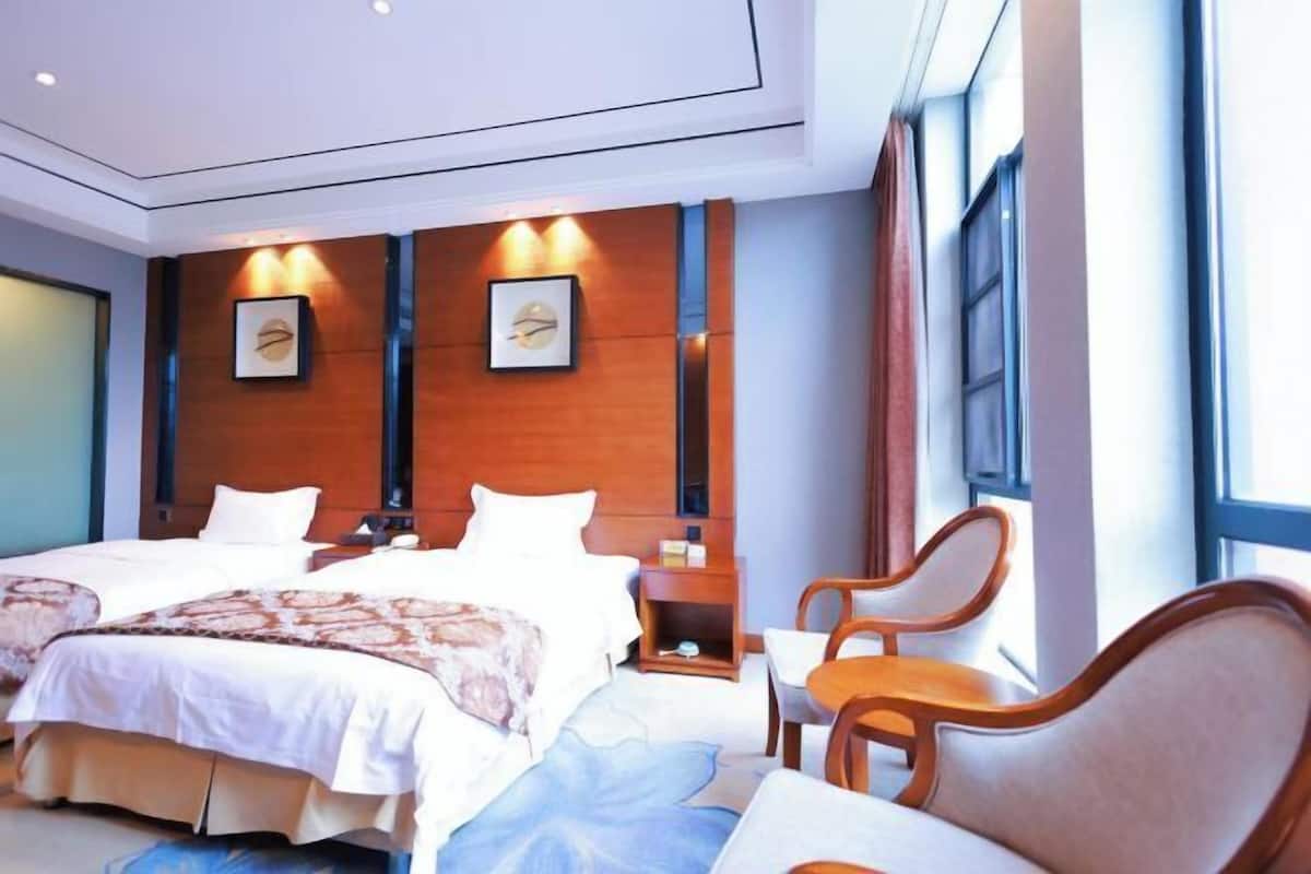 A hotel room with two beds, a wooden headboard, a small table with chairs, and framed artwork on the wall.