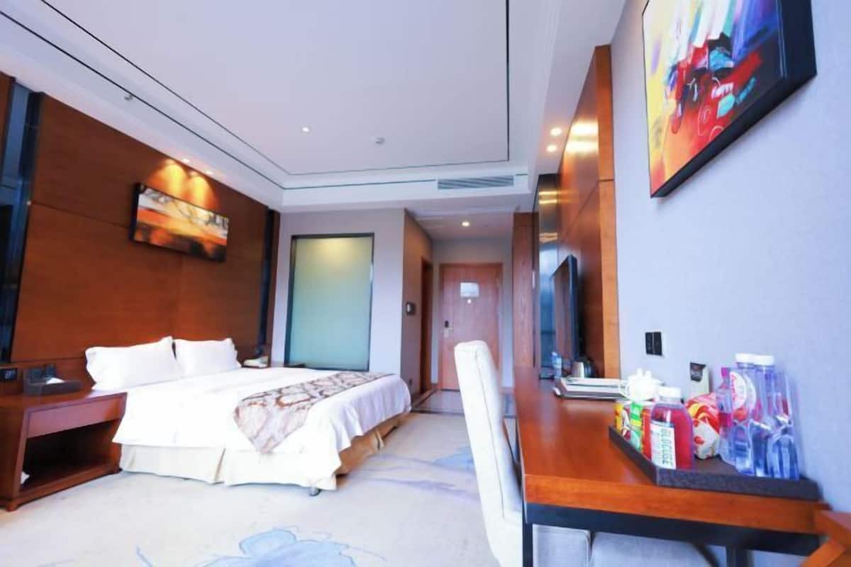 A hotel room with a bed, bedside table, desk, chair, and a wall-mounted TV.
