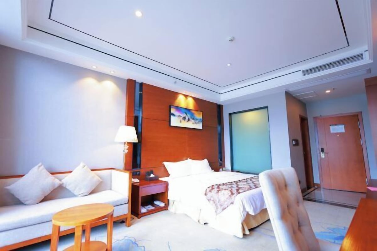 A hotel room with a bed, a sofa, a chair, a small table, and a TV.