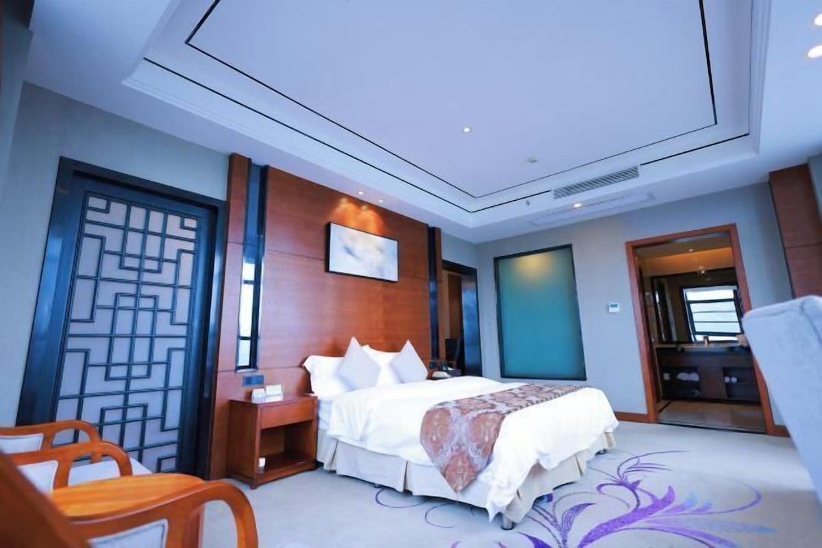 A hotel room with a bed, a desk, a chair, and a decorative wall panel.