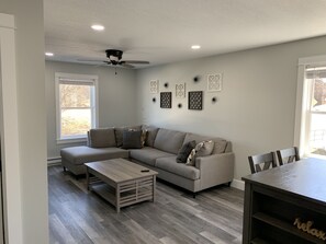 A living room with a sectional sofa, a coffee table, and a dining table with chairs. - Modern Apartment Fallsview in the Finger Lakes (Burdett)