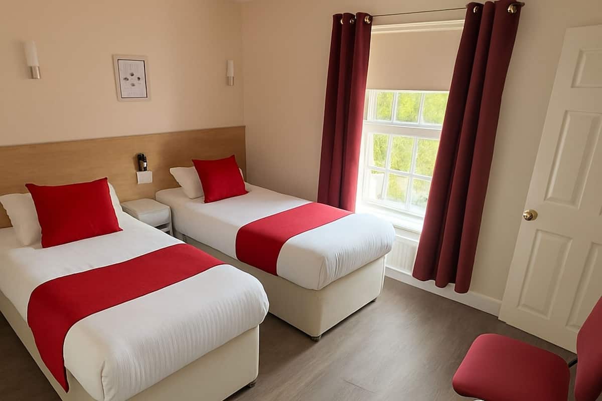 A hotel room with two beds, a red chair, a waste bin, and a window with curtains.