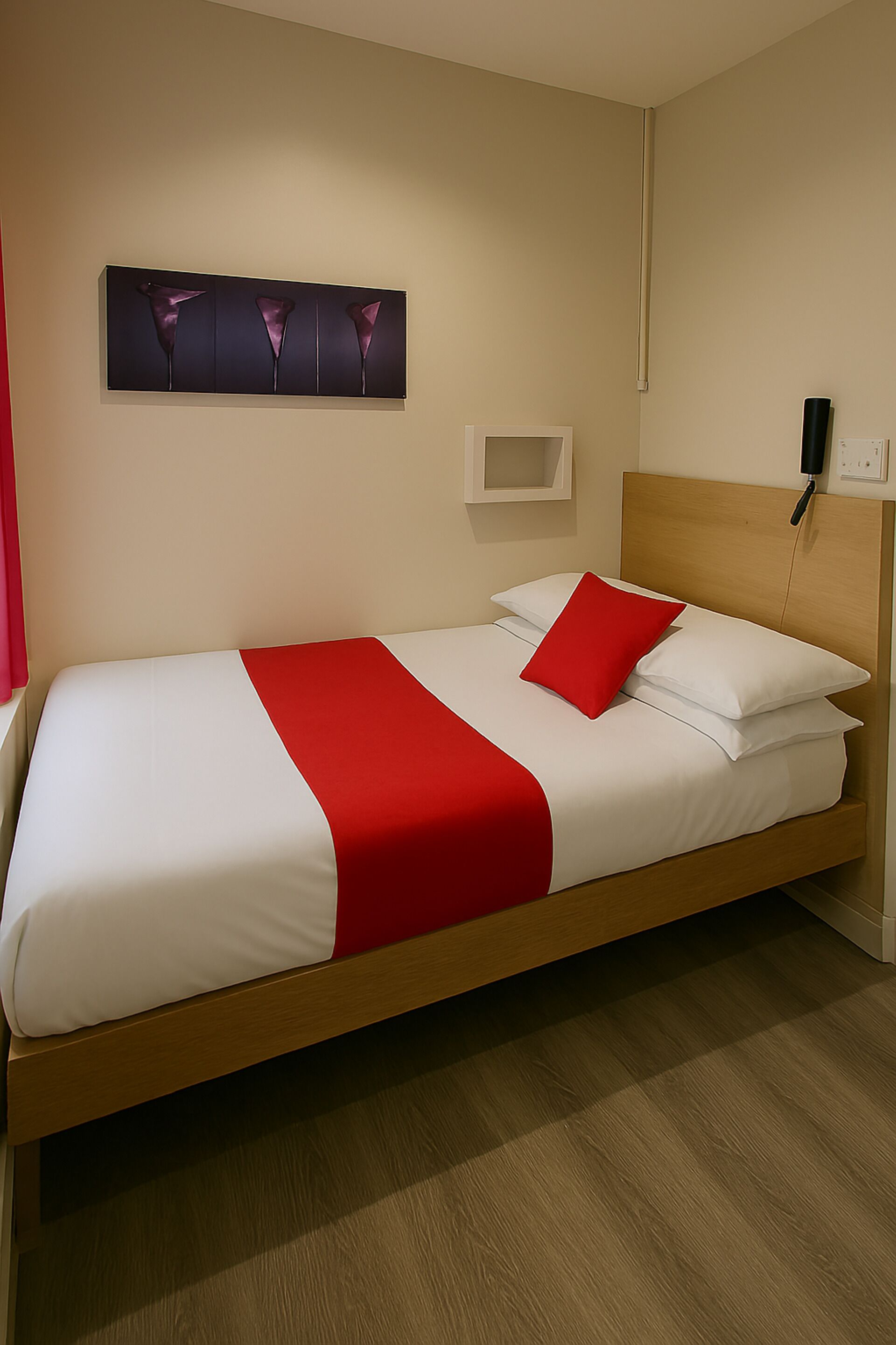 Een netjes opgemaakt bed met rode accenten, een houten hoofdbord en een kunstwerk aan de muur erboven.