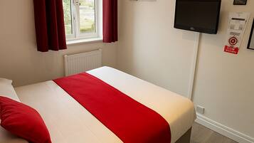 A neatly made bed with red and white bedding, a window with red curtains, a mounted television, and a framed picture on the wall.