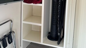 A room with a white wardrobe, a flat-screen TV, a standing heater, and a metal rack with black straps. - The Railway Sleeper Lodge  (Colchester)