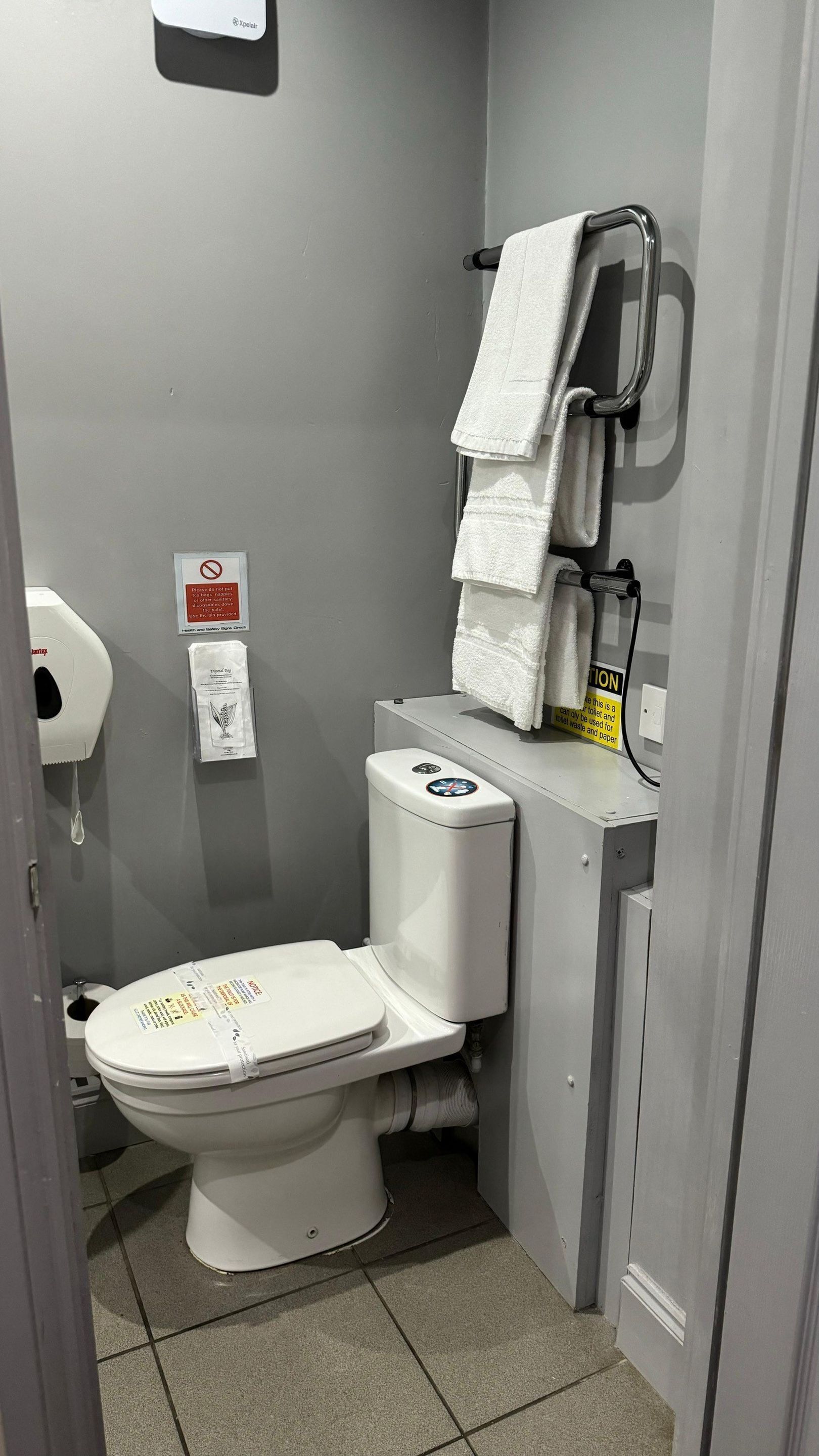Um banheiro pequeno e compacto, com vaso sanitário, secador de mãos e dispensador de toalhas de papel.