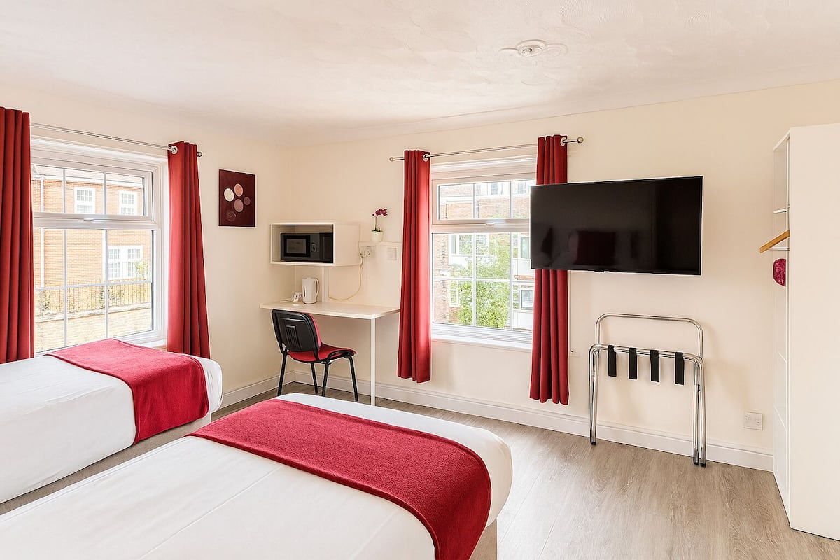 A hotel room with two beds, a desk with a chair, a TV, and a window with curtains.