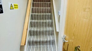 A narrow stairway with striped carpet, a wooden door with a plaque, and a warning sign on the wall. - The Railway Sleeper Lodge  (Colchester)