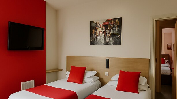 A hotel room with two beds, red and white bedding, a mounted TV, and a painting on the wall. - The Railway Sleeper Lodge  (Colchester)
