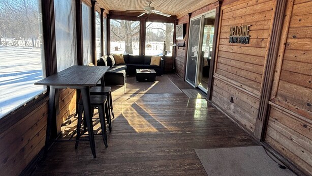 A wooden interior with a table and chairs, a ceiling fan, and a sign that reads 'WELCOME TO THE PARCH.' - The Yellow Farm (Spring Green)