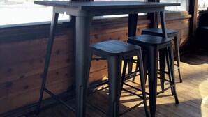 A wooden interior with a table and bar stools, large windows, and a view of trees and snow outside. - The Yellow Farm (Spring Green)