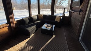 A cozy cabin interior with a sectional sofa, a coffee table, and large windows offering a view of a snowy landscape. - The Yellow Farm (Spring Green)