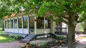 A house with a covered porch, a stone pathway, and a tree in the foreground. - The Yellow Farm (Spring Green)