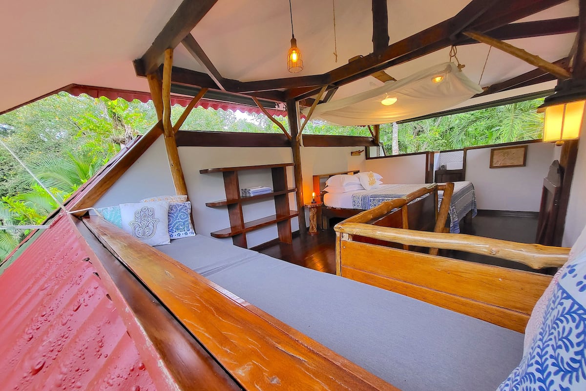 Eine Holzterrasse mit einem Bett und einem kleinen Tisch, umgeben von einer Holzbrüstung.