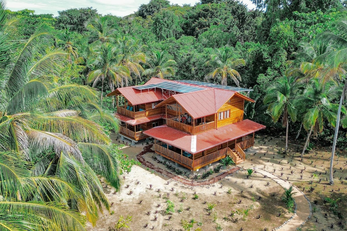 Ein zweistöckiges Holzhaus mit rotem Dach, umgeben von üppiger tropischer Vegetation.