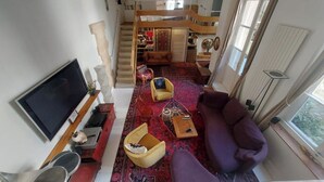 Een ruime woonkamer met een grote televisie, een bank, een rood tapijt en een trap naar een verdieping erboven.