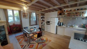 Een kleine keuken met witte kastjes, een koelkast, een magnetron en een spoelbak. Er is een eettafel met stoelen en een vloerkleed met dessin.
