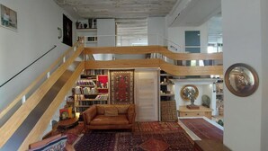 Een ruime loft met een hoge plafond, een houten wenteltrap, een gezellig leeshoekje met een leren bank, en een verzameling boeken en decoratieve objecten.