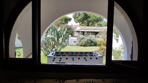 Ein Fenster mit bogenförmigem Blick auf einen Innenhof, der einen Tischkicker, einen Kaktus und ein Gebäude mit einem Ziegeldach zeigt.