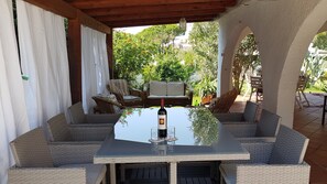 Une terrasse extérieure avec des meubles en osier, une table avec une bouteille de vin et une vue sur la verdure.