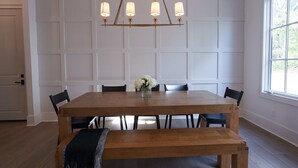 Een eetkamer met een houten tafel, vier stoelen, een bank, een kroonluchter en een raam met uitzicht.