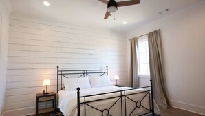 Een slaapkamer met een bed, twee nachtkastjes met lampen, een plafondventilator, een raam met gordijnen en houten paneelwanden.